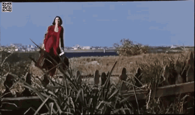 a woman in a red dress is walking through a field with a bag .