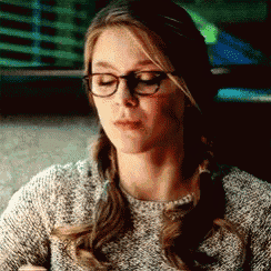 a woman wearing glasses and a sweater is looking down at something .