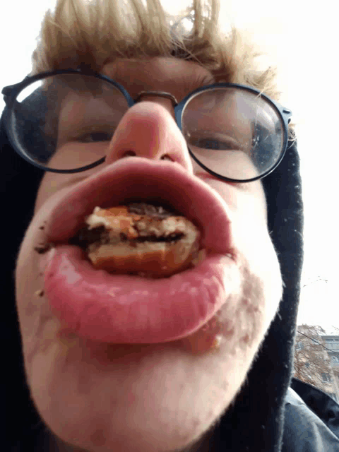 a person wearing glasses and making a funny face with food in their mouth