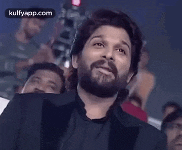 a man with a beard is smiling and laughing while sitting in front of a crowd .
