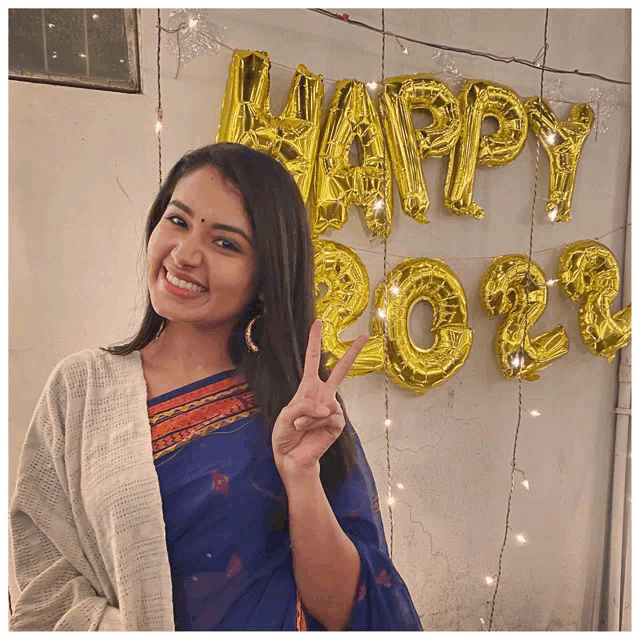 a woman giving a peace sign in front of balloons that spell happy 2022