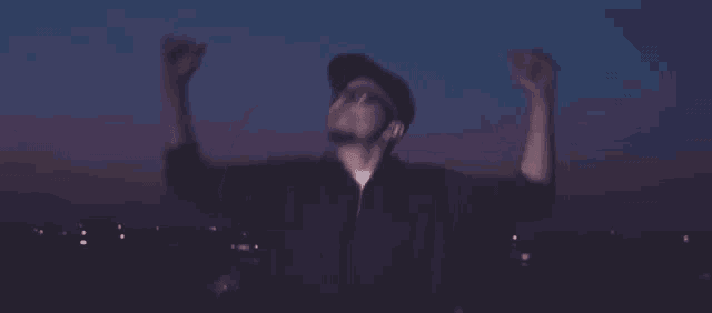 a man wearing a hat and glasses is dancing with his arms in the air at night .