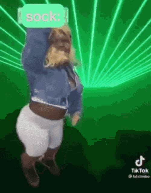 a woman in a denim jacket and white shorts is dancing in front of a green background .
