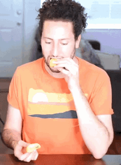 a man in an orange shirt is eating a piece of lemon