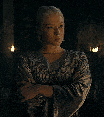 a woman with her arms crossed and her eyes closed stands in a dark room