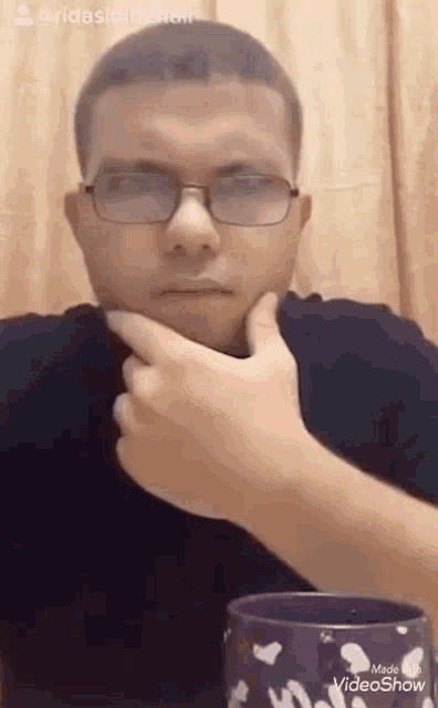 a man wearing glasses and a black shirt is sitting at a table with a purple cup .