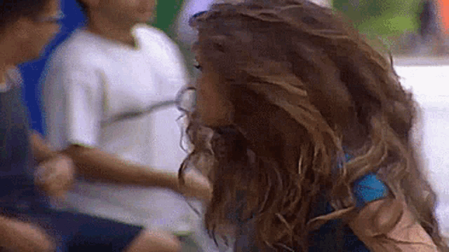 a woman with long curly hair is standing in front of a group of children .