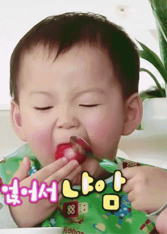a baby wearing a green bib is eating a strawberry with a spoon