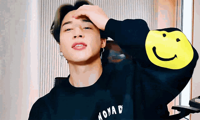 a young man wearing a black sweatshirt with a yellow smiley face on the sleeves .