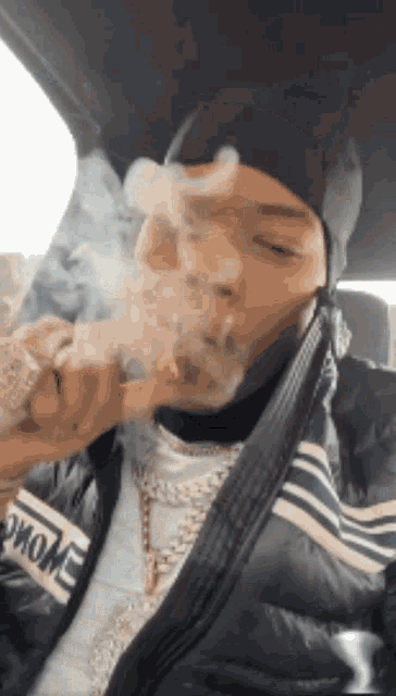 a man is smoking a cigarette in a car while wearing a jacket that says moncler on it .