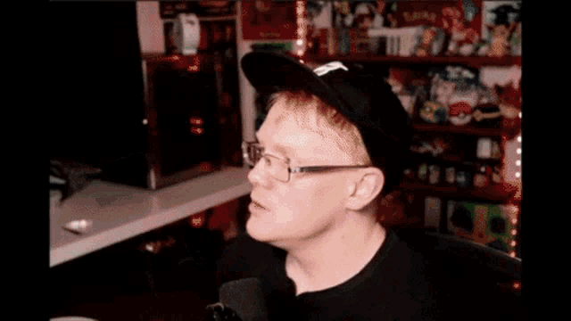 a man wearing glasses and a black hat is holding a remote control