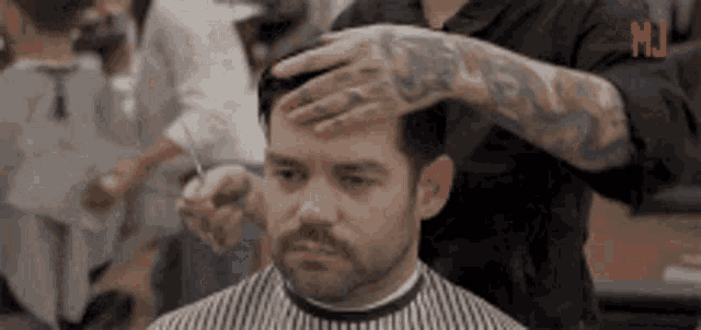 a man is getting his hair cut by a barber with a tattoo on his arm .