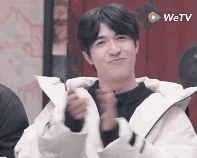 a young man wearing a white jacket and a black sweater is applauding .