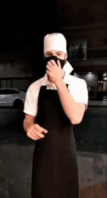 a man wearing a black apron and a white hat covering his face