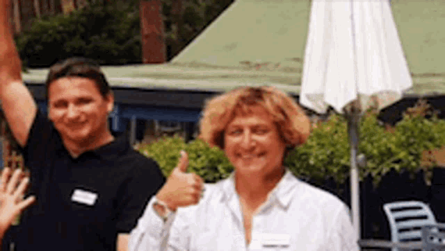 a man and a woman are standing next to each other giving a thumbs up sign .