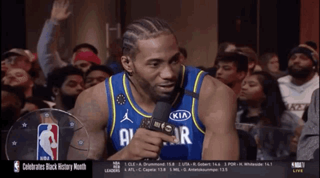 a basketball player wearing a kia jersey talks into a microphone in front of a crowd