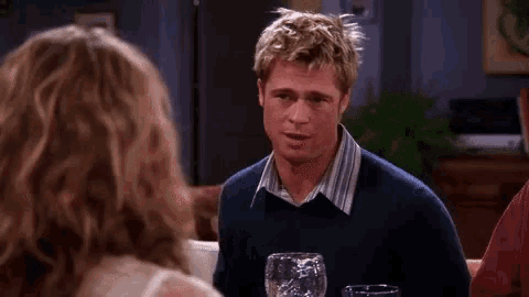 a man in a blue sweater is talking to a woman while sitting at a table .