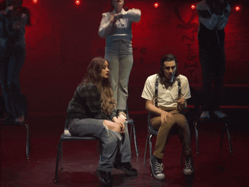 a man in suspenders sits next to a woman in a sweater