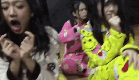 a group of girls are sitting on a couch and one of them is wearing a yellow sweater with a smiley face on it
