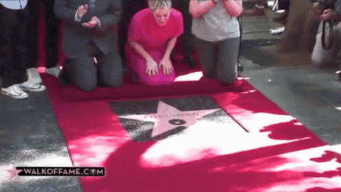 a woman kneeling on a red carpet with a walkofffame.com logo in the corner