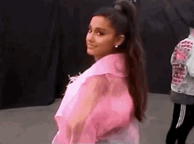 ariana grande is wearing a pink crop top and a pink ponytail .