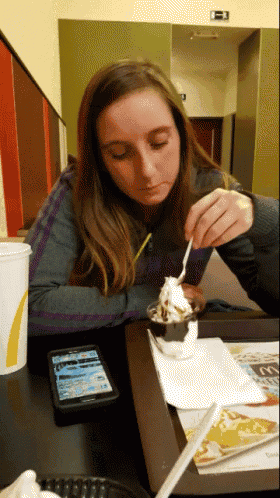 a woman sits at a mcdonald 's table eating ice cream and looking at her phone