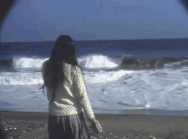 a woman is standing on a beach looking at the ocean waves