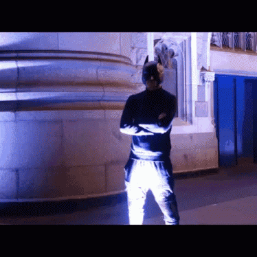 a man in a batman costume stands with his arms crossed