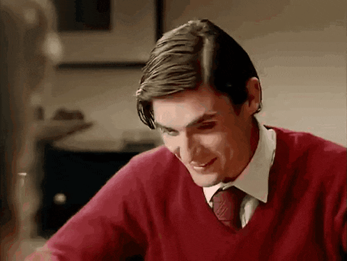 a man wearing a red sweater and tie is smiling while sitting at a table .