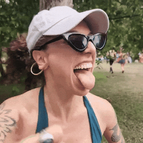 a woman wearing sunglasses and a hat is sticking out her tongue