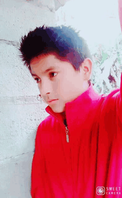 a young boy wearing a red jacket is taking a picture with the sweet camera