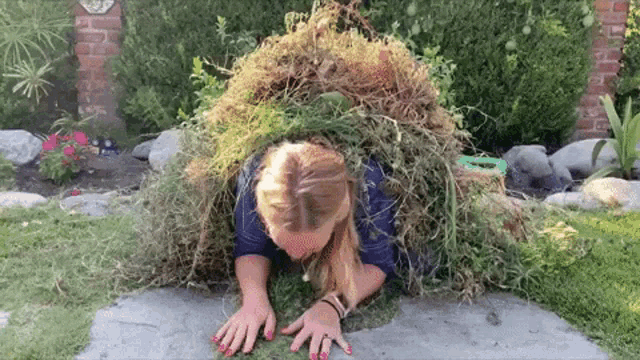 a woman is crawling under a pile of grass with a sign in the background that says ' a '