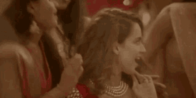 a group of women are standing around a woman in a red dress and talking to her .