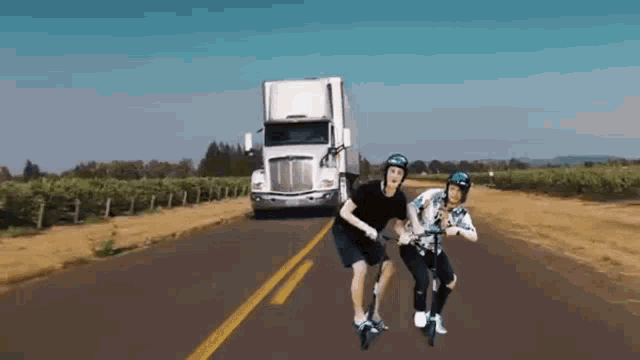 two people riding scooters on a road with a truck in the background