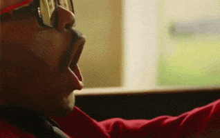 a man wearing glasses and a red shirt is yawning while sitting in front of a window .