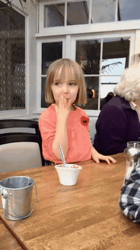 a little girl is sitting at a table with a bowl of food and a bucket