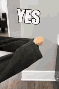 a person in a black suit is standing in front of a wall with the word yes written on it .
