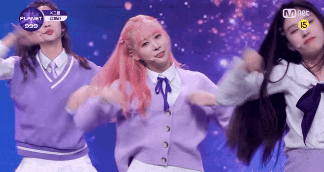 a girl with pink hair is dancing on a stage with two other girls .