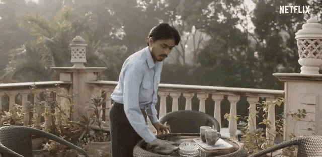 a man is standing next to a table on a balcony and cleaning it .