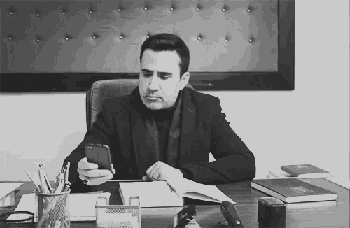 a man sits at a desk looking at his cell phone