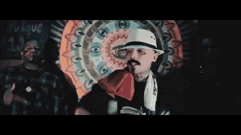 a man wearing a sombrero stands in front of a colorful wall with the word cualque written on it