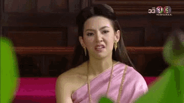a woman in a pink dress is sitting on a red couch making a funny face .