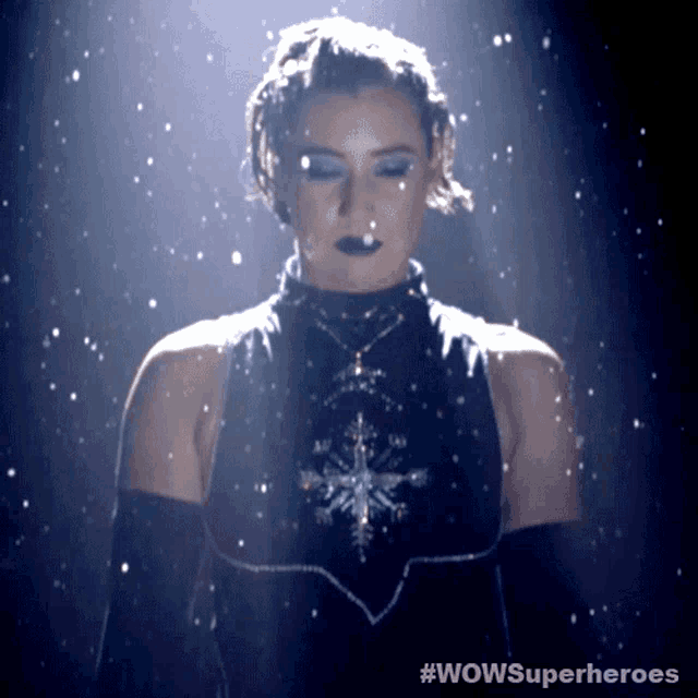 a woman in a black dress with a snowflake on her chest stands in front of a sign that says wowsuperheroes