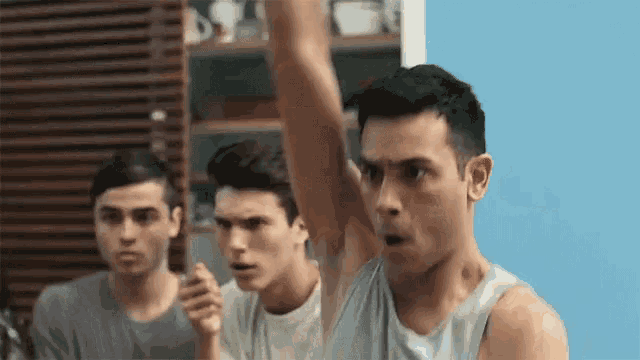 three young men are standing next to each other in a room and one of them is raising his arm in the air .