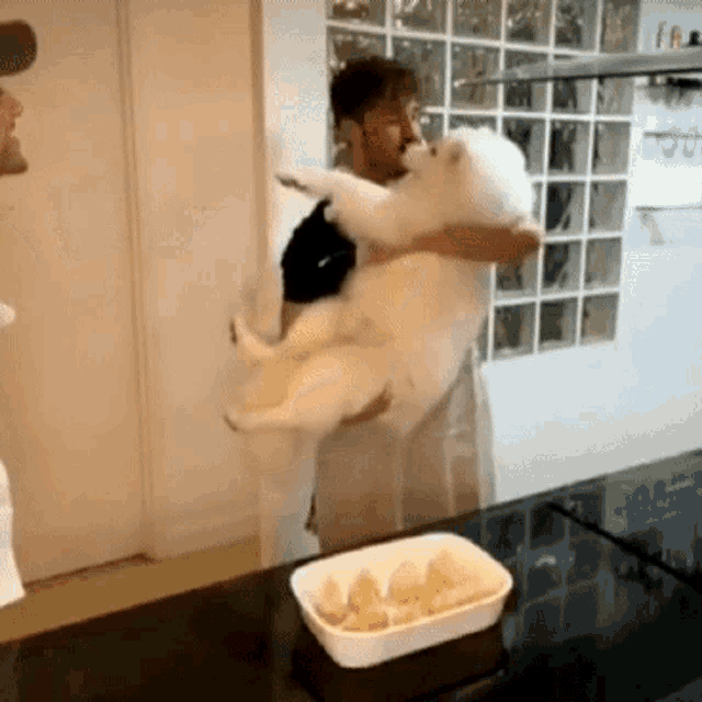 a man is holding a white dog in his arms in front of a tray of food .