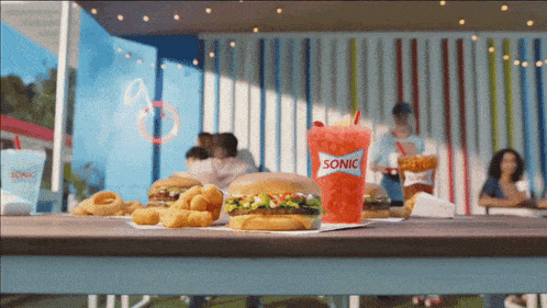 a sonic drink sits on a table with a hamburger and onion rings