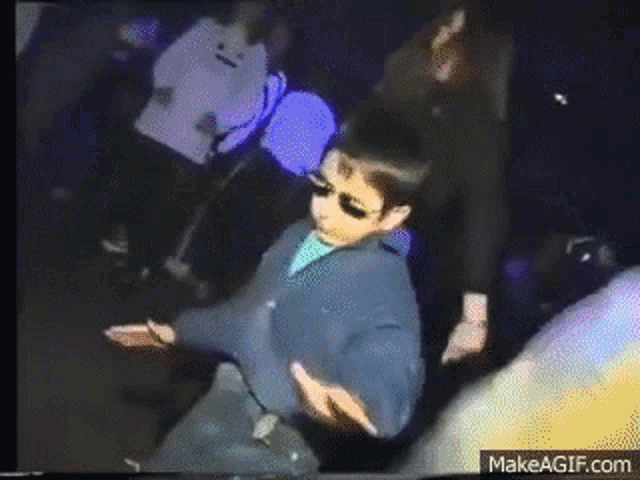 a young boy wearing sunglasses is dancing in a crowd of people .