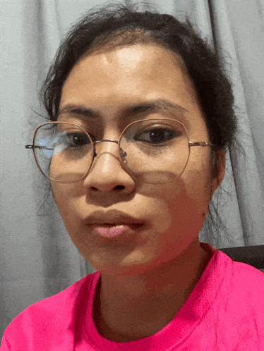 a woman wearing glasses and a pink shirt makes a funny face