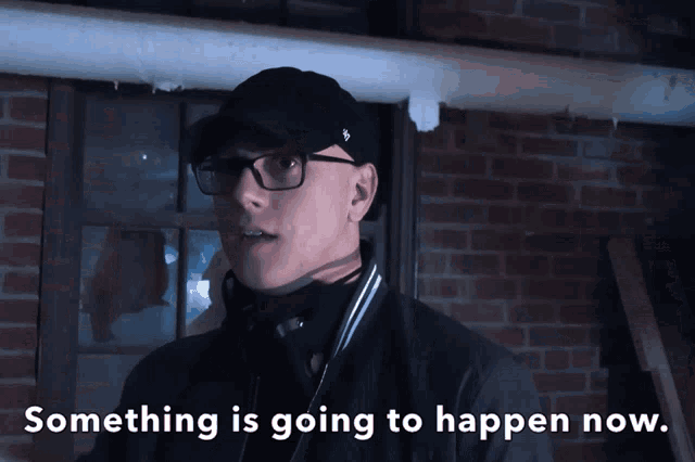 a man wearing glasses and a hat with the words something is going to happen now below him