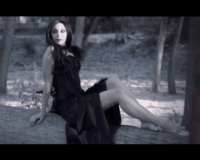 a woman in a black dress sits on a log in the woods